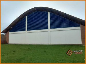 veneziana industrial Fachada em pintura eletrostática azul Del Rey aplicada em um ginásio poliesportivo tem como finalidade apresentar uma das possibilidades de aplicação do produto em um ambiente esportivo. A cor azul Del Rey utilizada na pintura eletrostática transmite elegância e modernidade, além de harmonizar com a maioria dos projetos arquitetônicos.A veneziana industrial Solution em pintura eletrostática azul Del Rey é ideal para o uso em ginásios poliesportivos, já que oferece uma ventilação natural adequada e uma iluminação natural que pode ser ajustada de acordo com as necessidades do espaço. A imagem exemplifica como o produto atua tanto em propriedades funcionais, contribuindo com a climatização e iluminação natural, como também em propriedades estéticas, trazendo harmonia e beleza ao ambiente do ginásio poliesportivo. Em resumo, a imagem mostra a veneziana industrial Solution em pintura eletrostática azul Del Rey como uma solução eficiente, prática e moderna para quem busca aliar conforto térmico, economia de energia elétrica e design sofisticado em ginásios e espaços poliesportivos.