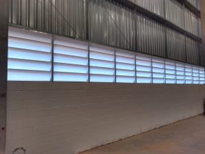 Imagem ilustrando a combinação de lanternins e venezianas em galpão industrial, promovendo ventilação natural e eficiência térmica.