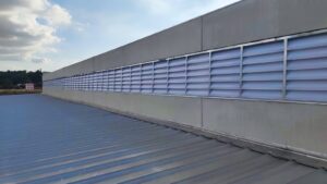 Foto tirada de um ângulo inferior das venezianas na OPUSPAC, evidenciando o espaçamento entre as aletas para a circulação do ar. O design favorece a exaustão natural do ar quente de dentro do galpão.