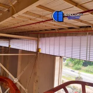 Fachada completa de galpão industrial equipada com venezianas Solution. A imagem destaca a extensão das lâminas instaladas na alvenaria, permitindo a entrada massiva de luz natural e a circulação de ar externa para o interior da fábrica.