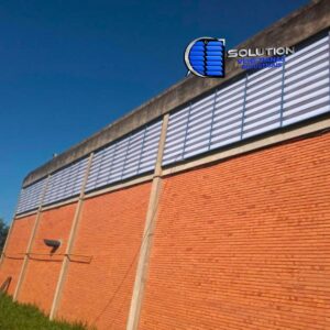 Registro de obra finalizada com venezianas industriais Solution em PVC branco leitoso. A imagem mostra o fechamento lateral de um galpão com aletas opacas que garantem ventilação permanente, privacidade interna e um acabamento estético uniforme na fachada.