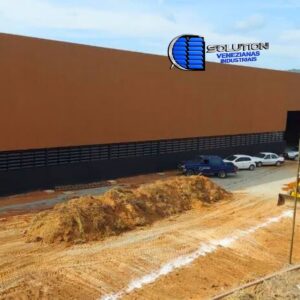 Fachada de galpão industrial com venezianas Solution em aço galvanizado com pintura eletrostática preta. A imagem destaca as lâminas metálicas foscas, proporcionando ventilação permanente e um design moderno e imponente para a estrutura.