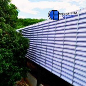 Fachada de galpão industrial com venezianas em policarbonato branco alveolar Solution. A imagem destaca a passagem de luz suave e difusa pelas aletas translúcidas, criando uma iluminação interna uniforme e sem sombras projetadas.