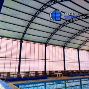 Fachada lateral de galpão industrial equipada com sistema de venezianas industriais Solution. A imagem ilustra a entrada de claridade natural e o fluxo de ventilação através das aletas, destacando a eficiência energética e o conforto térmico da edificação.