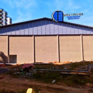 Fechamento de oitão de galpão industrial com venezianas Solution instaladas em formato triangular (grau), acompanhando a inclinação do telhado para exaustão de ar quente.