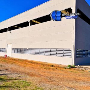 Fachada industrial com venezianas Solution em aço com pintura eletrostática cinza claro, destacando o acabamento uniforme e a integração estética com a estrutura metálica.