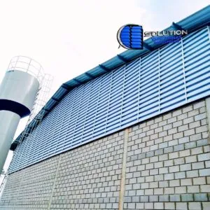 Fachada de galpão industrial destacando a instalação de venezianas Solution no oitão (fechamento triangular superior). A imagem mostra as aletas acompanhando a inclinação do telhado, garantindo a exaustão do ar quente acumulado na parte mais alta da estrutura.