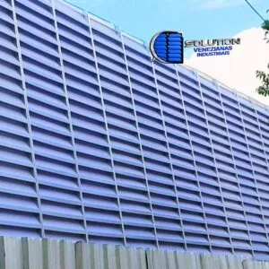 Fachada lateral de galpão industrial com sistema de venezianas Solution instaladas em toda a extensão. A imagem demonstra a entrada de luz natural e a abertura das aletas projetadas para promover a ventilação cruzada e renovação do ar interno.