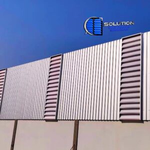 Detalhe de fachada industrial com venezianas Solution instaladas de forma intercalada entre telhas trapezoidais metálicas. A imagem mostra a integração perfeita entre o fechamento opaco e as aletas translúcidas, garantindo pontos estratégicos de ventilação e iluminação natural.