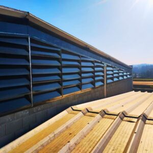 As venezianas em policarbonato alveolar fumê translúcido são projetadas para fachadas com alta incidência solar. A pigmentação fumê filtra a radiação direta, reduzindo o índice de ganho de calor solar (SHGC) e o ofuscamento interno. A estrutura alveolar composta por paredes duplas cria um colchão de ar isolante, otimizando a inércia térmica do galpão. O sistema garante ventilação permanente por convecção e alta resistência a impactos, com proteção contra raios UV em ambas as faces.