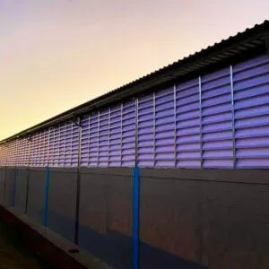 Fachada de galpão industrial do setor alimentício com venezianas Solution em policarbonato branco leitoso translúcido. A imagem mostra as aletas instaladas em grandes vãos, proporcionando iluminação natural difusa e ventilação permanente para controle de temperatura interna.