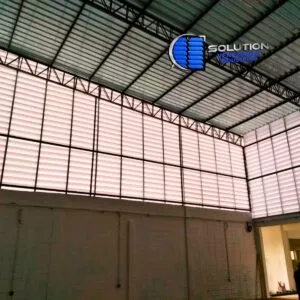 Fachada de galpão da indústria alimentícia com venezianas Solution em policarbonato branco leitoso translúcido. A imagem mostra as aletas brancas garantindo iluminação natural difusa e ventilação permanente para controle de temperatura interna.