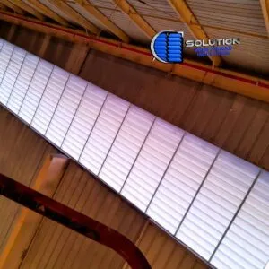 Fachada de galpão industrial do setor alimentício com venezianas Solution em policarbonato branco leitoso translúcido. A imagem mostra as aletas instaladas de forma contínua, permitindo a entrada de luz difusa e garantindo a ventilação necessária para a segurança alimentar.