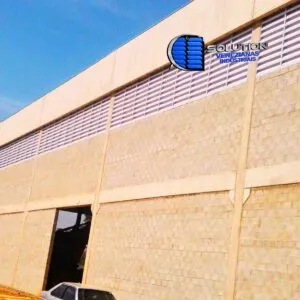 Fachada de galpão industrial com venezianas Solution em policarbonato alveolar branco leitoso. Lâminas translúcidas instaladas em estrutura metálica para difusão de luz solar e ventilação permanente.