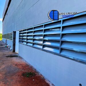 Fachada industrial com venezianas Solution em aço com pintura eletrostática cinza claro, destacando o acabamento uniforme e a integração estética com a estrutura metálica.