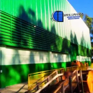Fachada industrial com venezianas Solution em aço galvanizado com pintura eletrostática verde, integrando ventilação permanente à identidade visual da empresa.