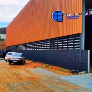 Detalhe de fachada industrial com venezianas Solution em aço com pintura eletrostática preto fosco. A imagem destaca o acabamento acetinado das aletas metálicas, que oferecem ventilação permanente com um design elegante e contemporâneo.