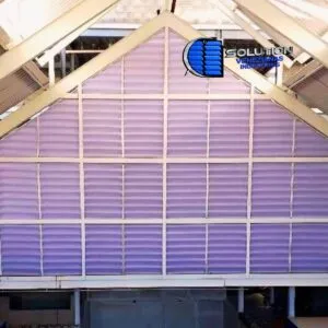 Fachada de galpão industrial com venezianas Solution instaladas no oitão (fechamento triangular superior). A imagem mostra as venezianas cortadas em grau, acompanhando perfeitamente a inclinação do telhado para exaustão natural do ar quente.