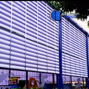 Fachada da área da piscina da Escola Objetivo em Indaiatuba - SP, com instalação de venezianas industriais Solution em policarbonato alveolar. A imagem mostra as lâminas translúcidas que cercam o ambiente aquático, permitindo a entrada de luz natural e a ventilação necessária para dispersar o vapor de cloro.