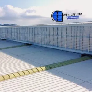 Vista detalhada de um lanternim industrial equipado com venezianas Solution em policarbonato branco translúcido. A imagem mostra a estrutura na cumeeira do telhado, permitindo a saída do ar quente e a entrada de luz zenital suave no galpão.