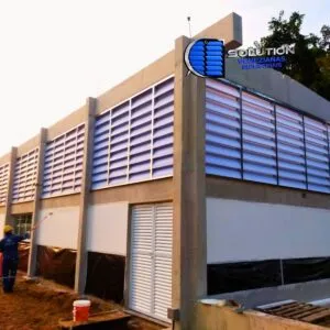 Fachada industrial com venezianas Solution em policarbonato branco alveolar. A imagem destaca a superfície translúcida que difunde a luz solar de forma uniforme, eliminando sombras e pontos de calor no interior do galpão.