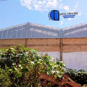 Fechamento de oitão de galpão industrial com venezianas Solution instaladas em formato triangular (grau). A imagem mostra o corte preciso das aletas acompanhando a inclinação do telhado para exaustão natural do ar quente