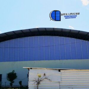 Fachada curva de ginásio poliesportivo com venezianas industriais Solution em policarbonato alveolar branco leitoso. As venezianas foram fabricadas em formato de arco, acompanhando a arquitetura da cobertura e proporcionando iluminação zenital translúcida e ventilação natural para a quadra