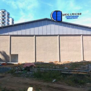 🖼️ Texto AlternativoFechamento de oitão em galpão industrial com venezianas Solution instaladas em formato trapezoidal/triangular, acompanhando a inclinação do telhado para exaustão de ar quente.