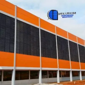 Fachada industrial com venezianas Solution em policarbonato alveolar fumê translúcido, destacando o controle de brilho solar e a ventilação permanente.
