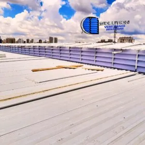 Nossas Obras Vista do telhado industrial com lanternim equipado com venezianas Solution em policarbonato alveolar. A imagem destaca a estrutura elevada na cobertura, permitindo a saída do ar quente e a entrada de luz zenital difusa no galpão.