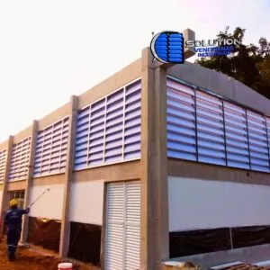 Fechamento lateral de galpão industrial com venezianas Solution. A imagem destaca a entrada de luz natural abundante através das aletas translúcidas, iluminando todo o interior da fábrica sem o uso de lâmpadas elétricas durante o dia.