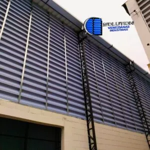 Análise de Performance:Ganho Lumínico: Nossas venezianas translúcidas possuem alto índice de transmissão de luz difusa, garantindo os níveis de iluminância exigidos pelas normas técnicas (ABNT) para ambientes fabris, sem gerar pontos de calor.Conforto Térmico: Através do cálculo de vazão de ar das aletas, promovemos a renovação constante do volume de ar interno. Isso reduz a temperatura ambiente e, consequentemente, a carga térmica sobre máquinas e colaboradores, otimizando a produtividade.Durabilidade: Fabricadas com materiais resistentes a raios UV e corrosão, as venezianas Solution mantêm sua performance óptica e estrutural por anos, evitando gastos com substituições frequentes.Resultado: Um galpão mais fresco, mais claro e com custos operacionais drasticamente reduzidos.