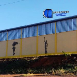 Fechamento de galpão industrial com venezianas Solution. O sistema utiliza aletas translúcidas para maximizar a entrada de luz natural e aberturas fixas para ventilação permanente, reduzindo o uso de lâmpadas e climatizadores.